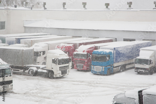 Trucks loading at warehouse and transport terminal. Parking in severe winter weather storm. Prohibition of traffic in heavy snow