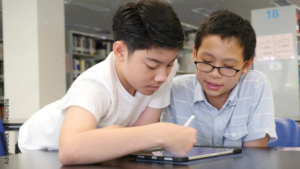 Young asian boys sitting in library and using tablet computer together. Young asian boys sitting in library and using tablet computer together.
