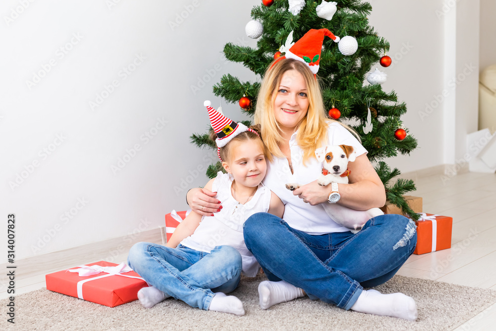 Cheerful mother with her daughter and jack russell terrier dog sitting near the Christmas tree Cheerful mother with her daughter and jack russell terrier dog sitting near the Christmas tree