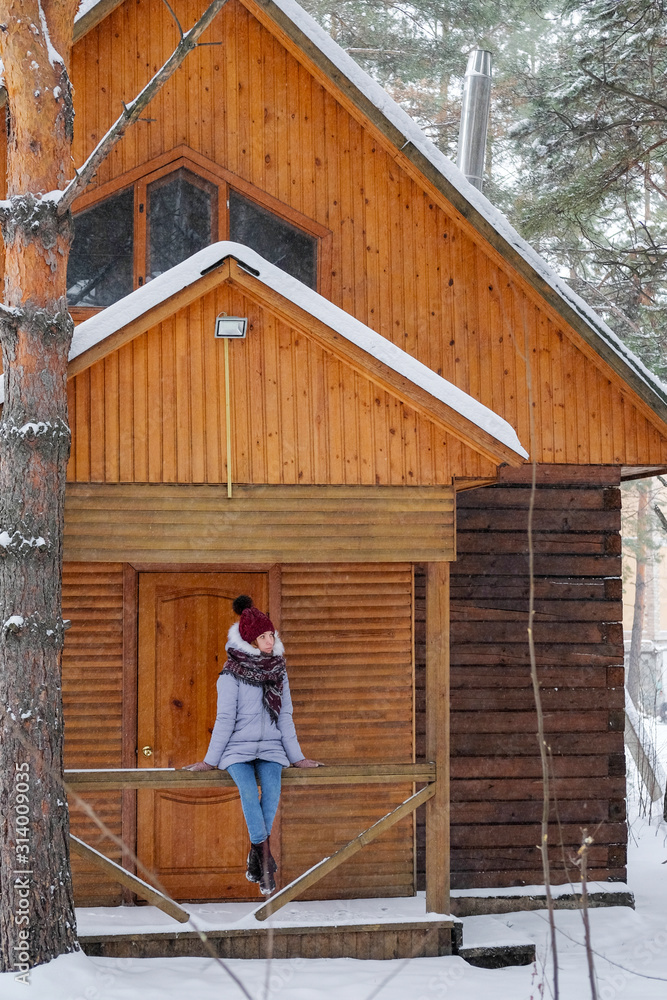 custom made wallpaper toronto digitalWoman sitting on snowy porch wooden rustic cottage in the winter woods. Portrait of a girl in a warm gray coat and burgundy knit scarf.