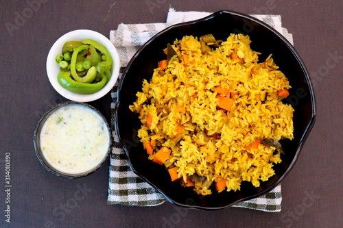 ndian Vegetable Pulav or Biryani made using Rice and vegetables like peas, carrots, beans. served with raita and saute peas, capsicum bowl.