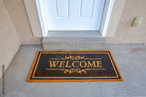 Black and brown Welcome doormat by the doorstep of home with white front door photo