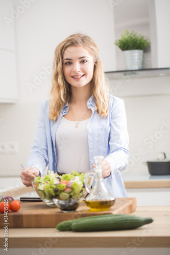 Young happy blonde girl preparing healthy salad in home kitchen