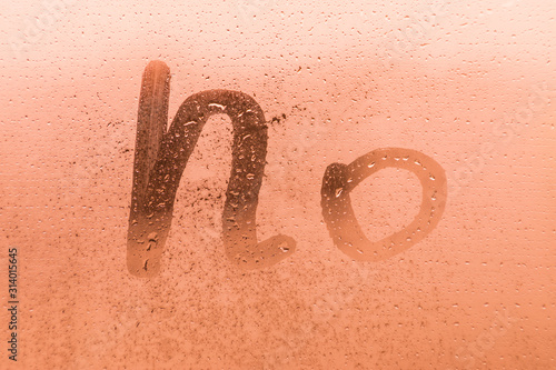 The creative inscription no on the orange or pink evening or morning window glass with drops 
