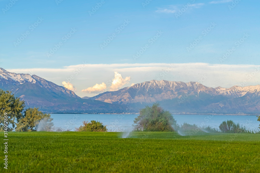 Green grass irrigated by sprinklers with lake and snowy mountain in background