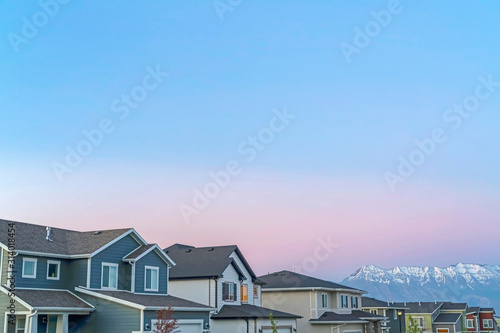 Fototapeta Exterior of homes and mountain with snowy peak against cloudy blue sky at sunset