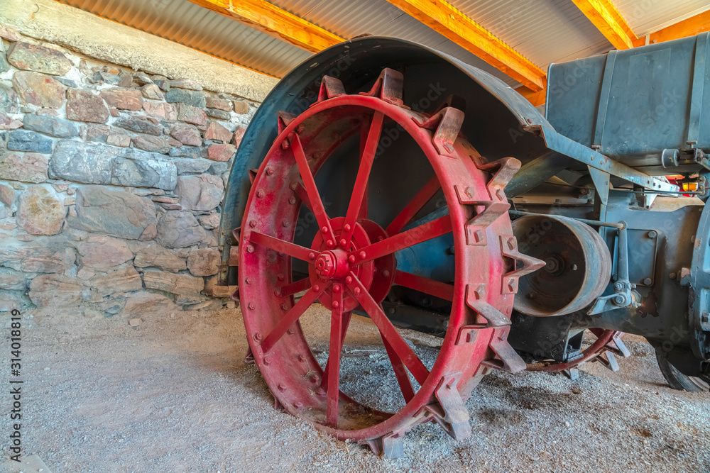 Red wheel rim of an and vintage tractor against stone wall of a farm barn