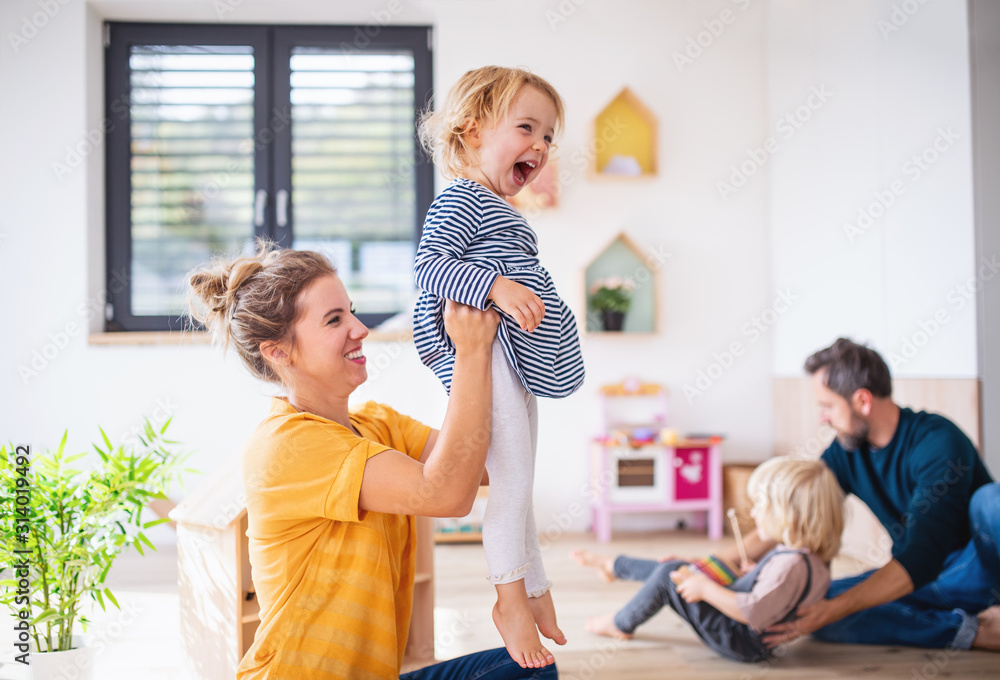 Young family with two small children indoors in bedroom having fun. - obrazy, fototapety, plakaty 