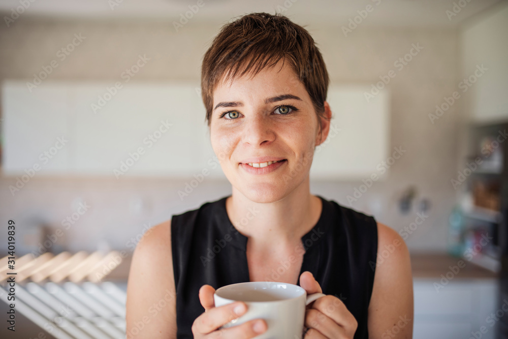 Front view of young woman with coffee standing indoors at home. Front view of young woman with coffee standing indoors at home.