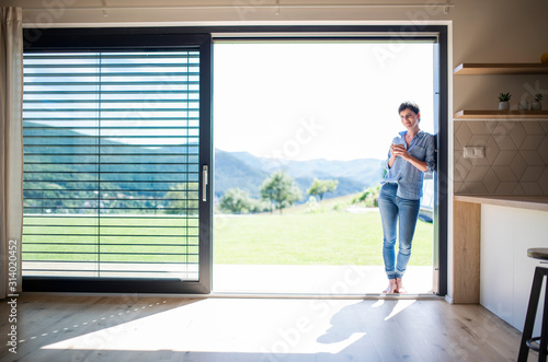 Front view of young woman with coffee standing by patio door at home. © Halfpoint