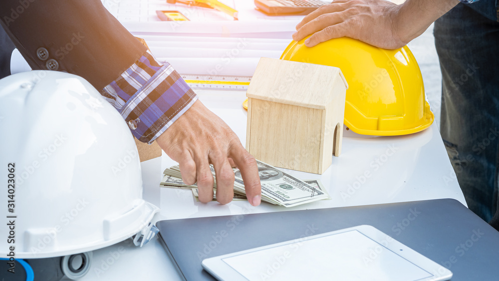 An engineer hat and a house with orange lights and a man holding a dollar on the table