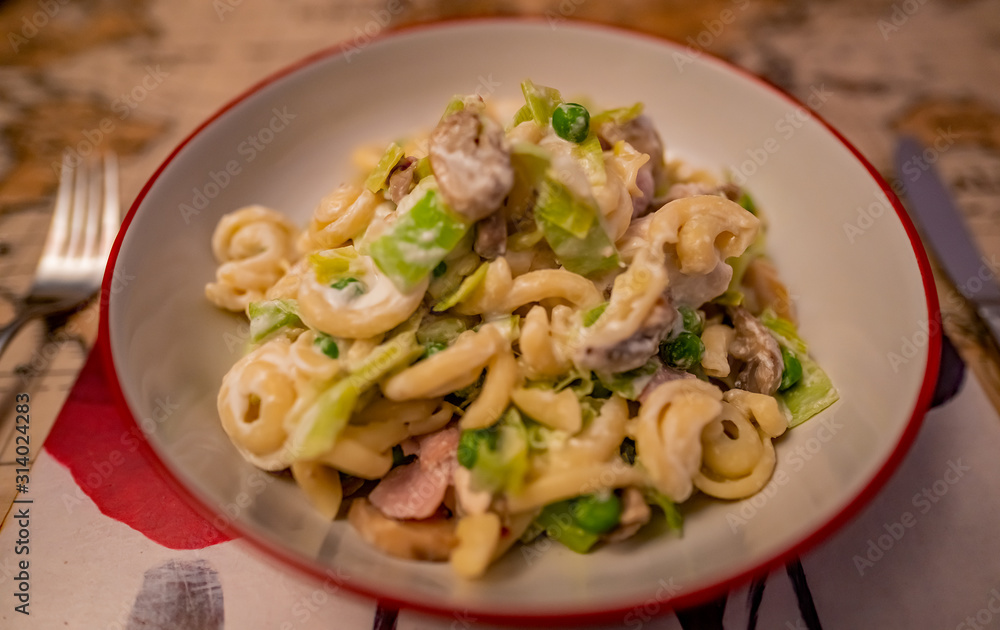 Selective focus of a leek, chicken and bacon pasta dish on a placemat on a dining table with a soft focus knife and fork Selective focus of a leek, chicken and bacon pasta dish on a placemat on a dining table with a soft focus knife and fork