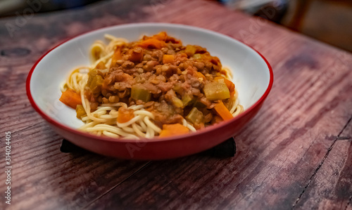  Close up of bowl of lentil spaghetti bolognese on a plain wooden background
