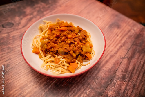 Close up of bowl of lentil spaghetti bolognese on a plain wooden background