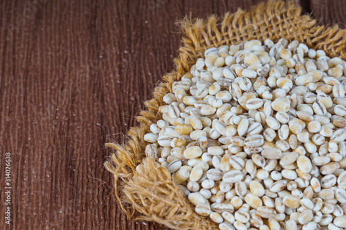 Close up on raw barley wheat placed on brown sack over wooden background