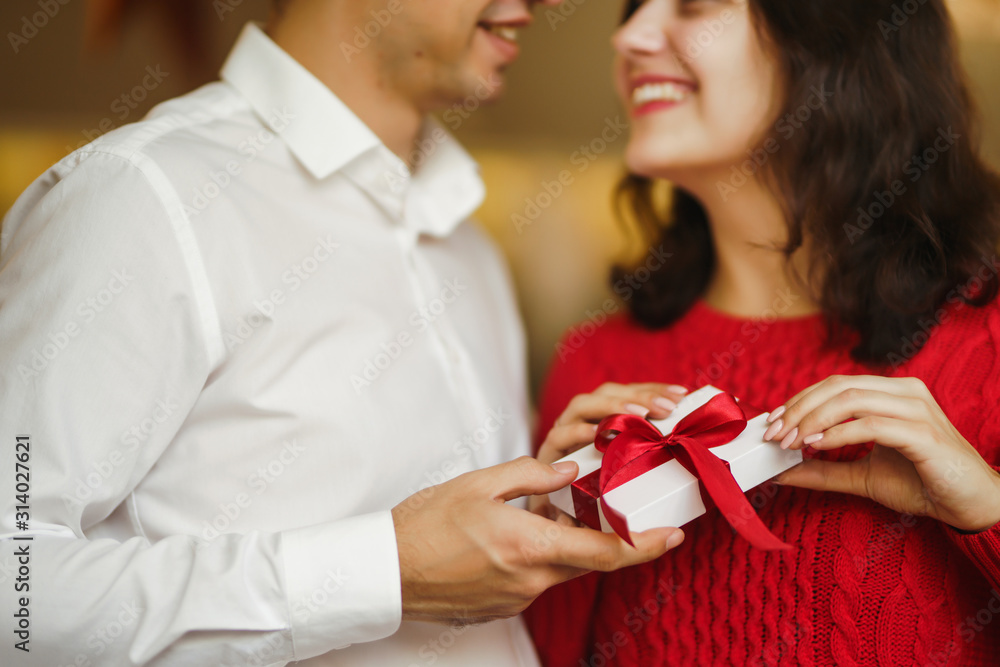 Valentine's Day, holiday and surprise concept. Man gives to his woman a gift box with red ribbon. A loving couple cuddles and celebrating Valentine's Day in the restaurant. Lovers give each other gift Valentine's Day, holiday and surprise concept. Man gives to his woman a gift box with red ribbon. A loving couple cuddles and celebrating Valentine's Day in the restaurant. Lovers give each other gift