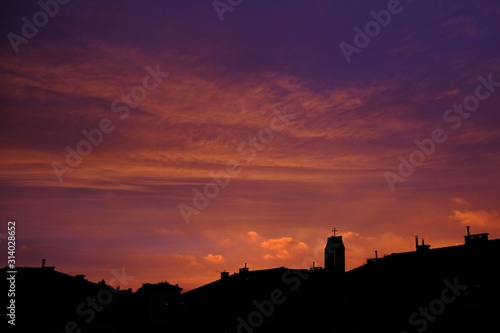 A wonderful sunrise over the city, looking like a burning sky. Black silhouettes of city buildings and church tower.