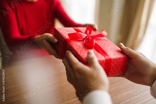 Valentine's Day, holiday and surprise concept. Man gives to his woman a red gift box. A loving couple celebrating Valentine's Day in the restaurant. Lovers give each other gifts.