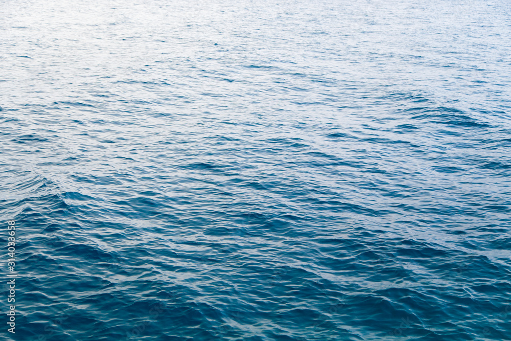 Clear water texture in blue. Background of the ocean and the sea backlit by the sun. Clear water texture in blue. Background of the ocean and the sea backlit by the sun.