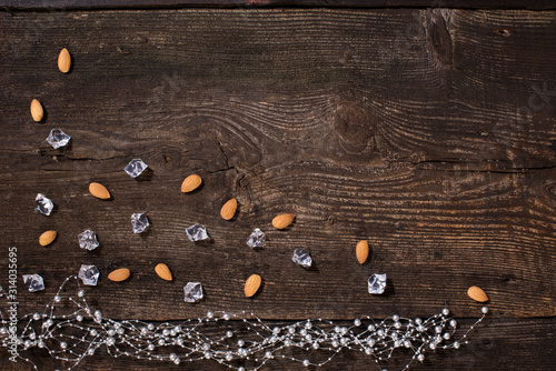 Almond, ice cubes and silver chain (garlands) on brown, old wooden plank arranged in frame