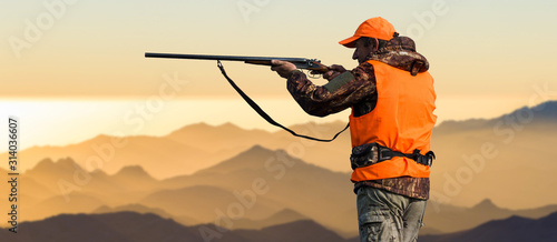 Silhouette of a hunter on the background of the morning red dawn. Stands at the ready with a gun.  © Mountains Hunter
