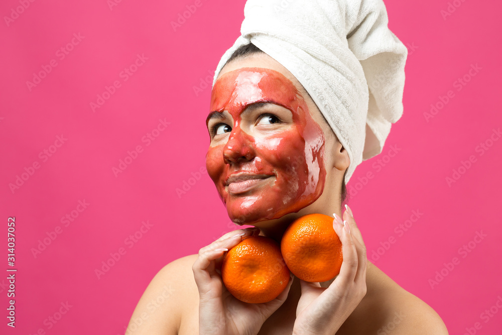 Beauty portrait of woman in white towel on head with red nourishing mask on face. Skincare cleansing eco organic cosmetic spa relax concept. A girl stands with her back holding an orange mandarin. Beauty portrait of woman in white towel on head with red nourishing mask on face. Skincare cleansing eco organic cosmetic spa relax concept. A girl stands with her back holding an orange mandarin.