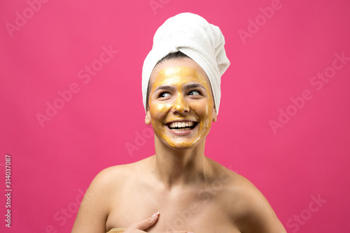 Beauty portrait of woman in white towel on head with gold nourishing mask on face. Skincare cleansing eco organic cosmetic spa relax concept.