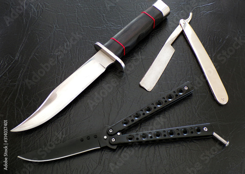 Cutting tools close-up on black leather background. A set of sharp knives. Bandit weapons. Weapons for murder. Bowie's hunting knife. Butterfly knife. Hand razor.