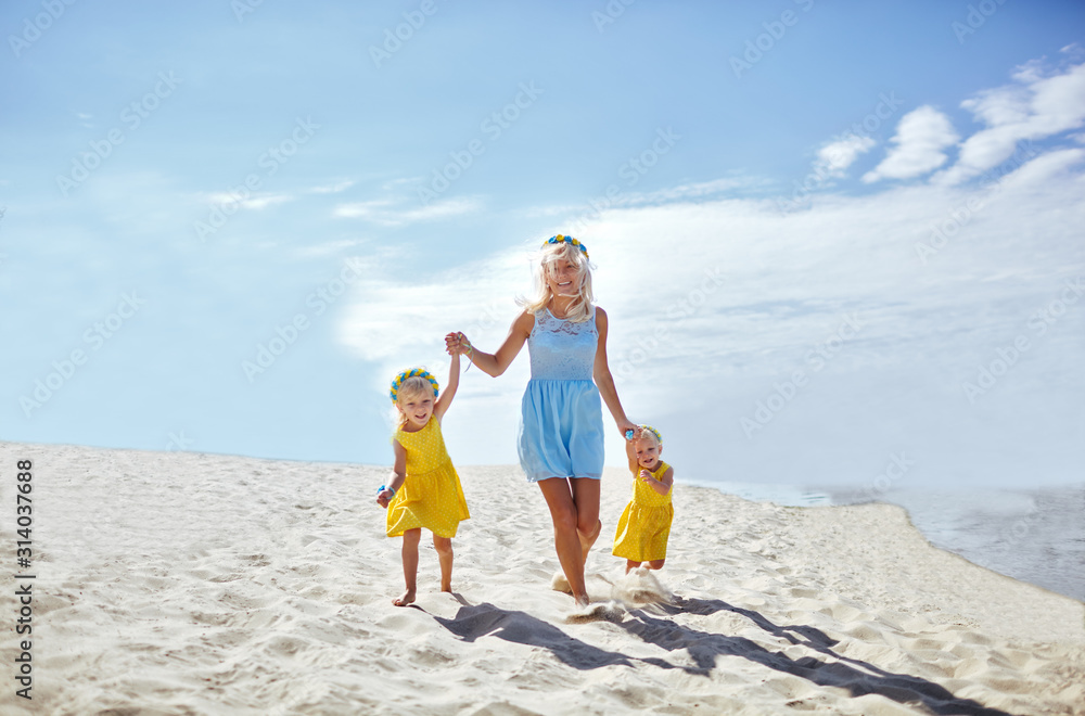 Happy family relaxing by the sea. Happy family resting at beach in summer.Young mother and her adorable little daughters on beach vacation. Concept of summer,childhood and leisure
