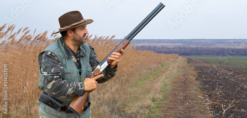 A hunter with a gun in his hands in hunting clothes in the autumn forest in search of a trophy. A man stands with weapon.