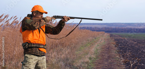 A hunter with a gun in his hands in hunting clothes in the autumn forest in search of a trophy. A man stands with weapon.