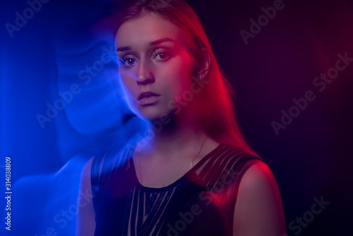 Blur effect of color traces. Portrait of a girl in a black dress. In the light of colored lamps contour blue and red. Fashion contemporary neon portrait. Adorable fashionable sexy model girl.