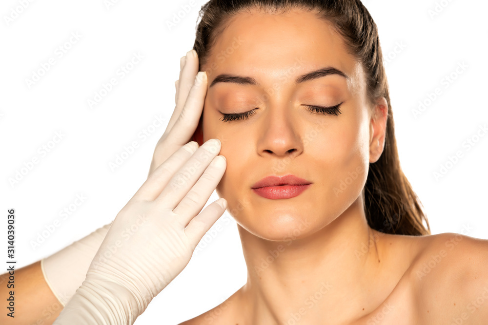 doctor's hands in gloves checks a face of young woman on white background