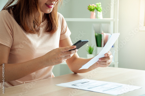 A woman uses a smartphone to scan the barcode to pay monthly phone bills after receiving an invoice sent to home. Online bill payment concept photo