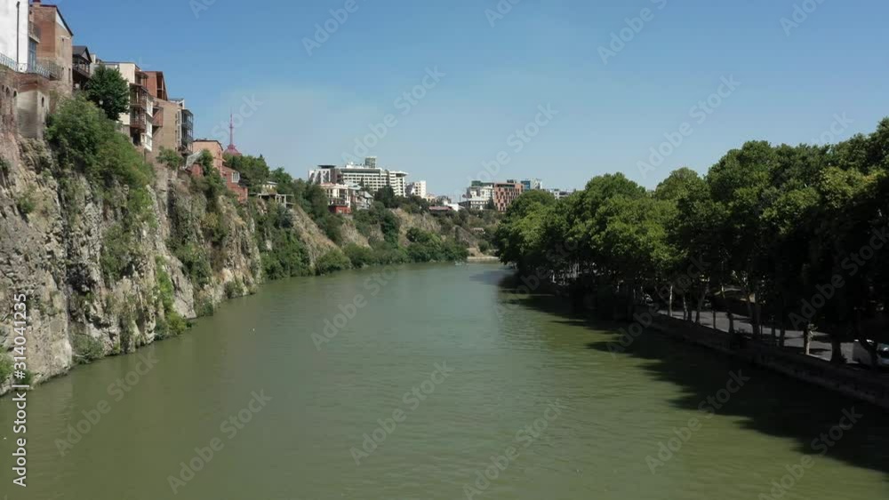 Aerial drone shot tilt up of Kura river and old houses near the water in Tbilisi. Old houses on the cliff at daylight in the summer. Drone flying over Tbilisi river Aerial drone shot tilt up of Kura river and old houses near the water in Tbilisi. Old houses on the cliff at daylight in the summer. Drone flying over Tbilisi river