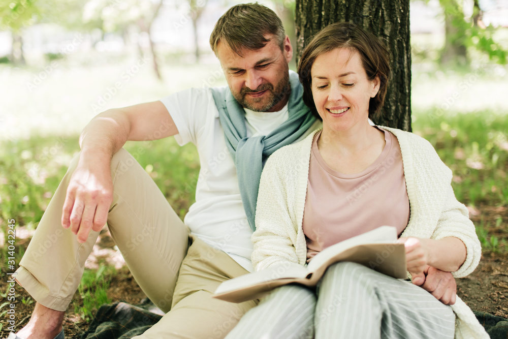 Middle-aged couple sit under a tree reading a book. Middle-aged couple sit under a tree reading a book.