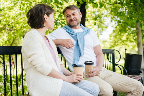 Couple sitting on the bench drinking coffee in the park.