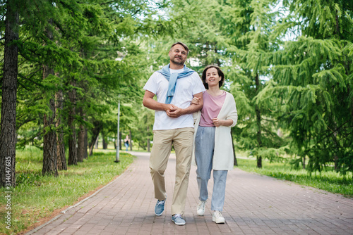 Middle-aged married couple walking in the park smiling.