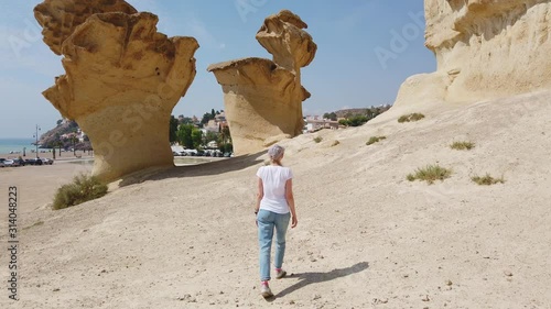 A steady shot of Girl walking through the desert near yellow futuristic rock. photo