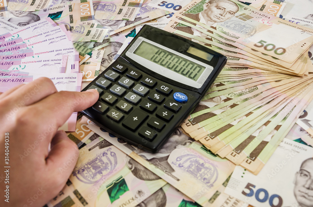 hand that prints on the calculator on the background of Ukrainian hryvnia. Million on the calculator scoreboard. hand that prints on the calculator on the background of Ukrainian hryvnia. Million on the calculator scoreboard.