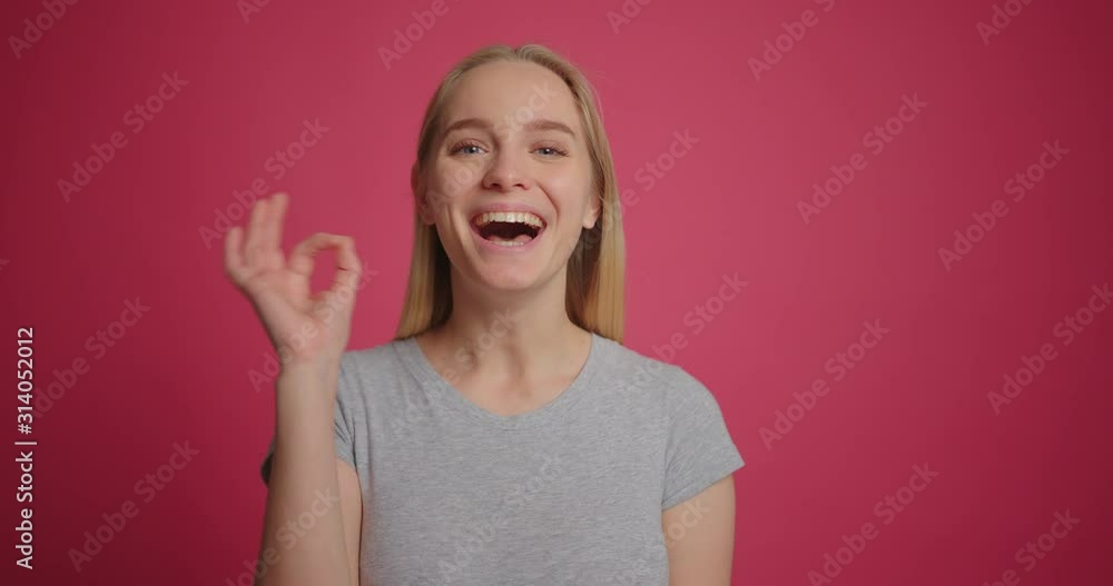 Happy blonde girl smiling and showing okay hand sign at pink wall slow motion Happy blonde girl smiling and showing okay hand sign at pink wall slow motion