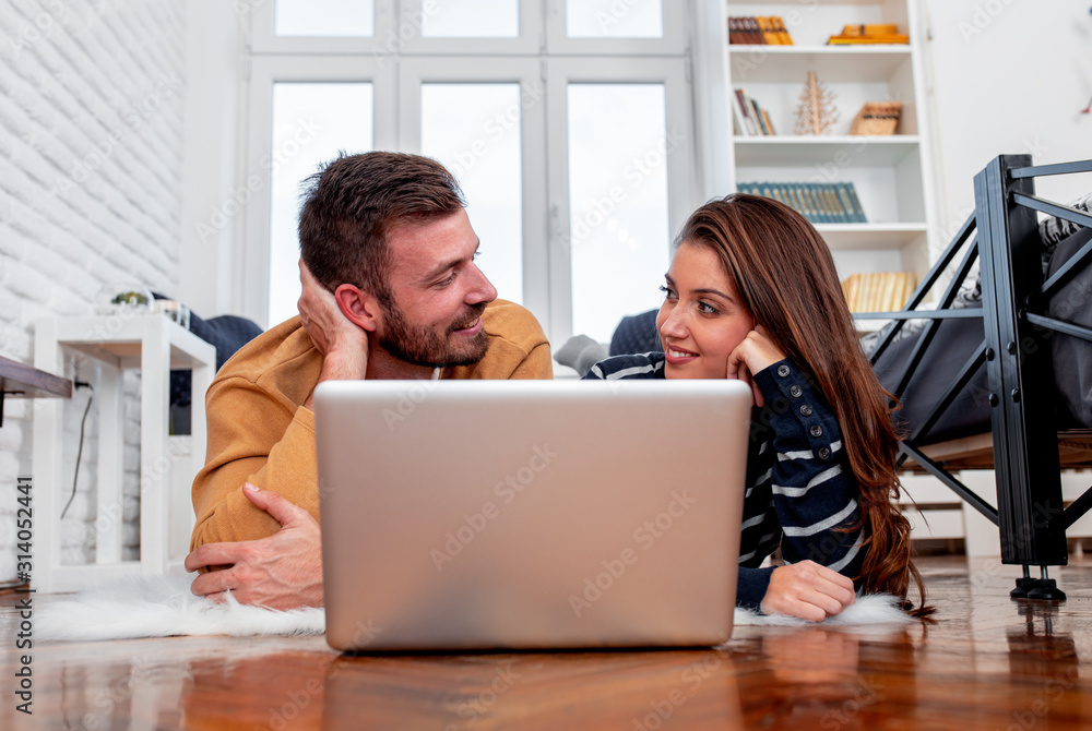 Young couple lying down on floor in apartment and using laptop. Young couple lying down on floor in apartment and using laptop.