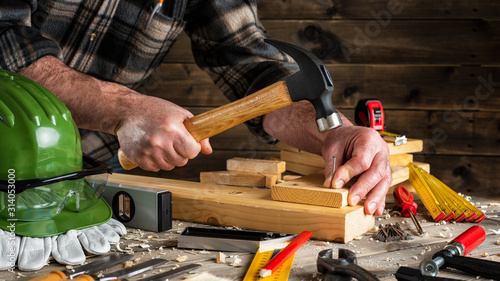 Close-up. Carpenter with hammer and nails fixes a wooden board. Construction industry, do it yourself. Wooden work table.