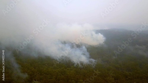 Aerial view of heavy smoke and fire engulfing eucalyptus tree forest during bush fire in Warragamba Australia, drone fast approach shot photo