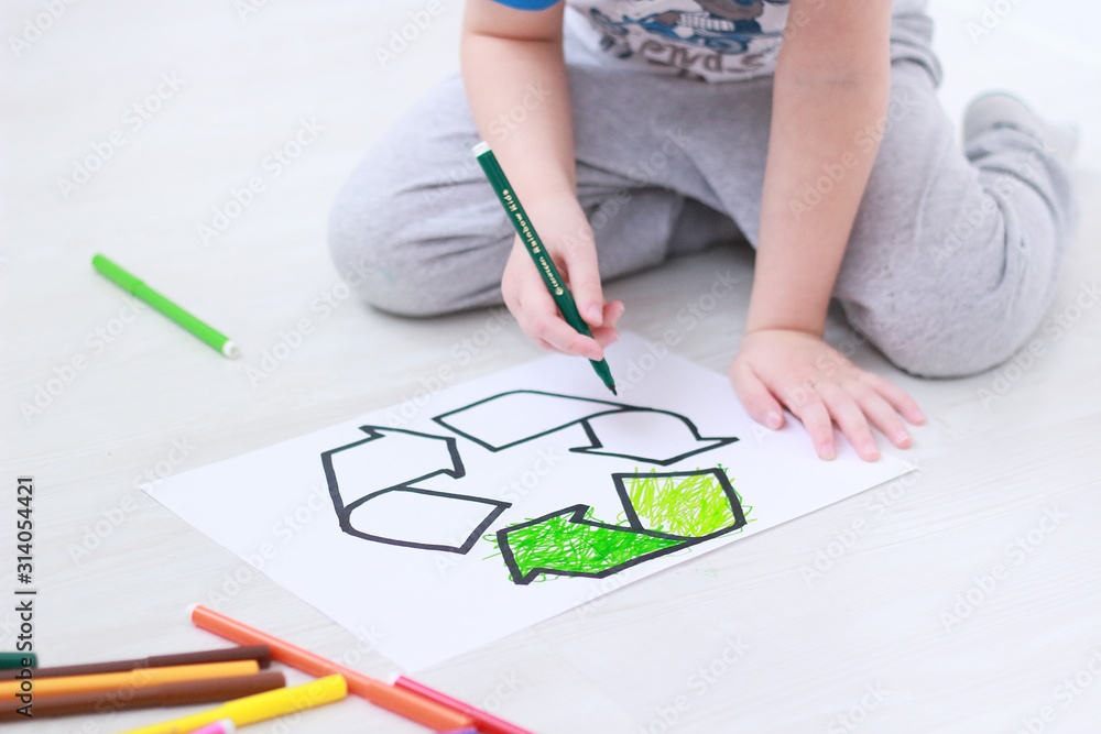 little boy colours with green felt-tip pen a recycling sign on the floor in the playroom. Ecology and environmental protection concept. selective focus little boy colours with green felt-tip pen a recycling sign on the floor in the playroom. Ecology and environmental protection concept. selective focus