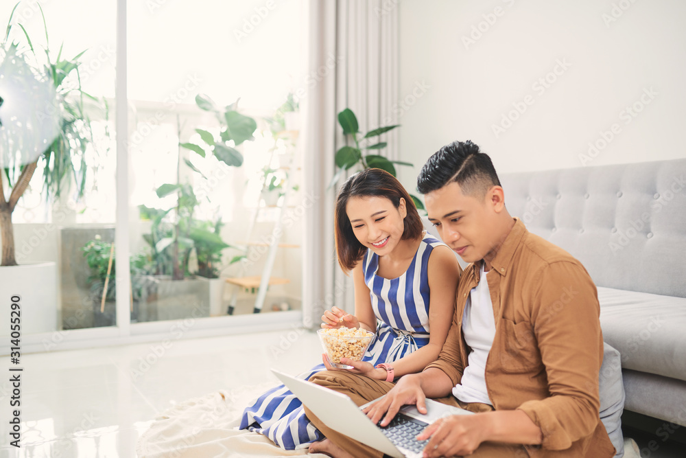 Young Asian couple watching a video on laptop in the living room Young Asian couple watching a video on laptop in the living room