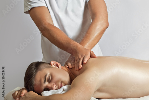 Massage therapist in a white T-shirt doing a back massage. The guy lies on the table on a white background. Manual therapy.