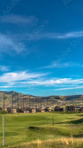 Vertical frame Golf course fairway and putting green with flagsticks under blue sky and clouds