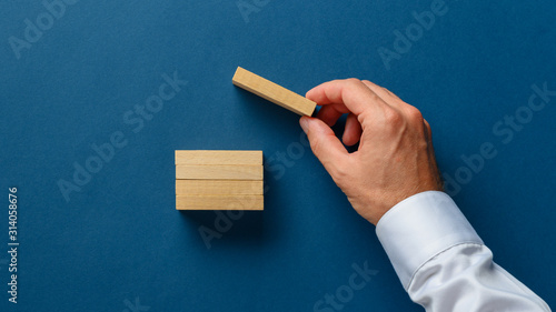 Hand of a businessman placing a wooden peg on top of stack of them photo