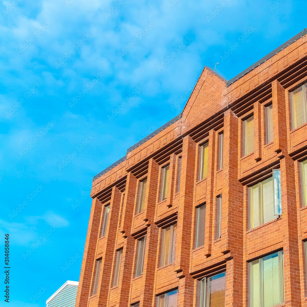 Square Commercial building with red brick wall viewed against blue sky and clouds